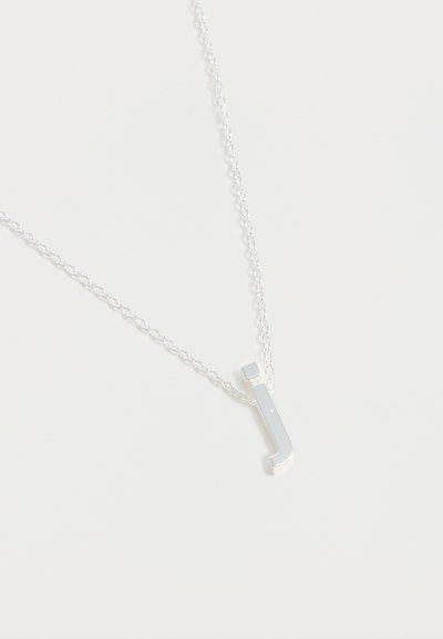 Collier à chaîne en argent avec un petit pendentif poli en forme de lettre « J » sur fond blanc uni.