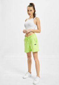 Hellgrüne Baumwollshorts mit elastischem Bund und Kordelzug, mit dem Schriftzug "DEF" in Schwarz. Kombiniert mit einem weißen, kurzen Tanktop.