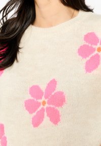 Cremefarbener Strickpullover mit großen rosa Blumenmustern und orangen Zentren, ausgestattet mit einem gerippten Halsausschnitt und einer weichen Textur.