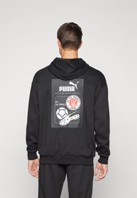 Felpa con cappuccio nera caratterizzata da una grafica con un pallone da calcio e una scarpa da calcio, marchiata con testo Puma e FC St. Pauli. Tessuto morbido e testurizzato.