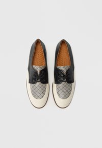 Chaussures à motifs noirs et blancs avec dessus en textile, semelle en caoutchouc beige et semelle intérieure marron. Dotées de lacets et d'un design à bout arrondi.