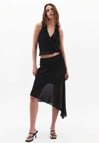 Zwart rimpelcrop top met een diepe V-hals, gecombineerd met een bijpassende asymmetrische rok met een transparante inzet en een aansluitende tailleband.