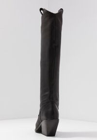 Czarne skórzane kozaki do kolan o gładkiej fakturze, lekko spiczastym czubku i niskim, ukośnym obcasie. Wyposażone w pętelkę na górze.