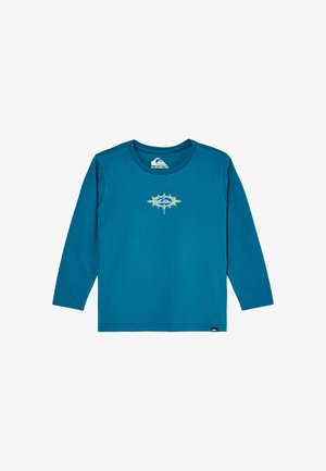 Chemise bleue à manches longues avec un col rond et un logo circulaire jaune et bleu au centre de la poitrine.