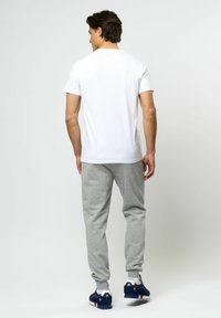 Vit kortärmad t-shirt som matchas med ljusgrå träningsbyxor med elastiska muddar. Skorna är marinblå med röda och vita detaljer.