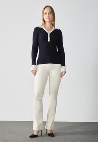 Navy ribbed long-sleeve top with cream collar and three-button placket; paired with cream flared pants and black pointed-toe heels.