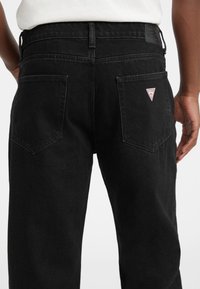 Melnas džinsa bikses ar brīvu piegriezumu. Raksturīgas īpašības: taisns griezums, divas aizmugurējās kabatas un trijstūrveida zīmola logotips.