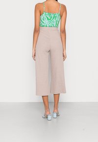 Light brown ribbed culotte pants with high waist and loose fit, paired with a green and white patterned top and light blue block-heeled shoes.