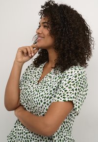 Blusa a maniche corte bianca con motivo astratto verde e blu notte, caratterizzata da un design a V e una vestibilità rilassata. Tessuto morbido.