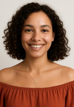 Gul vedhæng på en fin kæde, med et cirkulært design, båret med en off-the-shoulder topp i rustfarve. Krøllet hår synligt.