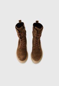 Brown suede ankle boots with textured laces, rounded toe, and a thick tan sole. Folded collar and side zipper detail.