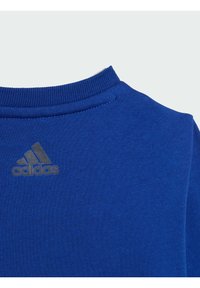 Felpa blu con collo a girocollo a coste, realizzata in tessuto morbido, con un piccolo logo grigio Adidas sul lato sinistro superiore.