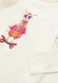 Lama in pinkem Jackett, orange Shorts, blauen Schuhen und blauen Sonnenbrillen, der auf einem roten Skateboard fährt, während es ein weißes langärmliges Shirt trägt.