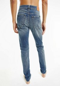 Hubené modré džíny z denimu se vybledlým povrchem, s koženou nášivkou na pásu a dvěma zadními kapsami s prošitím.