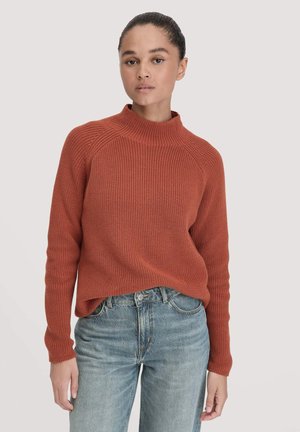 Geribde roestkleurige trui met een hoge kraag en lange mouwen, gecombineerd met lichtblauwe rechttoe-rechtaan jeans. De gezellige brei-textuur is duidelijk zichtbaar.