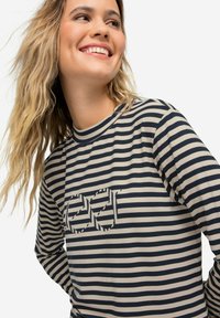 Dlouhý rukáv top s námořnickými a béžovými vodorovnými pruhy, s texturovaným grafickým designem na hrudi. Měkká bavlněná směsová tkanina.