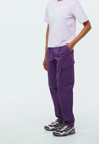 Purple cargo pants with side pockets, paired with a light purple short-sleeve shirt. Footwear features gray and black hiking shoes.