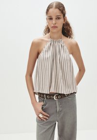 Top a halter color chiaro con strisce verticali, presenta un collo arricciato e una vestibilità ampia. Abbinato a jeans grigi e una cintura marrone con occhielli.