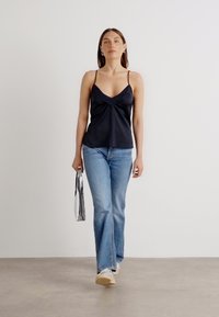 Svart satin cami med tynne stropper, med en vridd frontdetalj, paired med lyseblå vide jeans og en sølv metallisk veske.