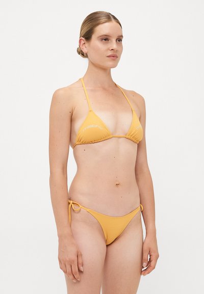 Dzeltenais bikini ar trīsstūrveida augšdaļu un regulējamiem sānos sasienamiem apakšpantiem, izgatavots no mīksta, gluda auduma ar minimālu šuvju detaļu.