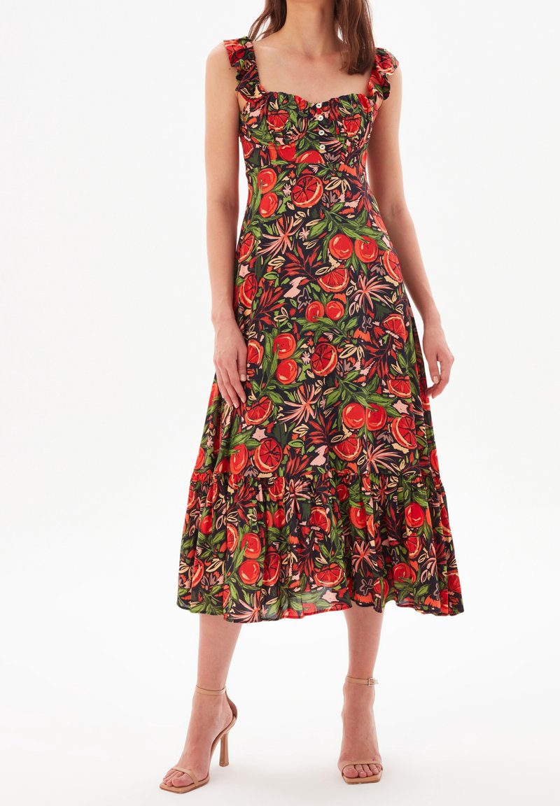 Blumenkleid in Midi-Länge mit Rüschenträgern, aus einem lebhaften schwarzen Stoff, der mit roten und grünen Früchte-Mustern verziert ist. Gestuftes Saumdesign.