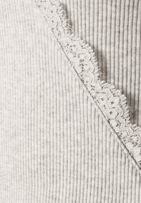 Gros plan sur un tissu gris clair côtelé avec une délicate bordure en dentelle florale blanche le long d'une couture diagonale.