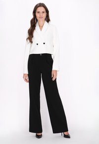 Dubbelzijdig witte blazer met hartvormige zwarte knopen, gecombineerd met hoge zwarte broeken en zwarte hakken. Eenvoudig, op maat gemaakt ontwerp.