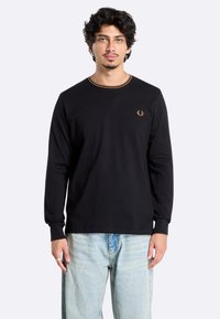 Zwarte langemouwen shirt met een ronde halslijn en een dunne bruine accent bij de kraag, met een gouden geborduurd logo op de linkerborst.