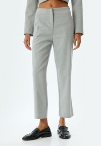 Pantalones gris a medida con corte recto y pliegues, que presentan una textura suave y un patrón sutil. Combinados con mocasines negros.
