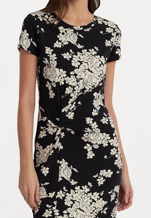 Robe noire à manches courtes avec motifs floraux blancs et un subtil détail froncé torsadé à la taille, portée par une femme.