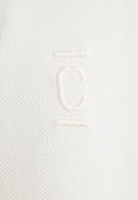 White knit fabric featuring a textured pattern with an embossed, contrasting logo detail. The design is minimalistic and clean.