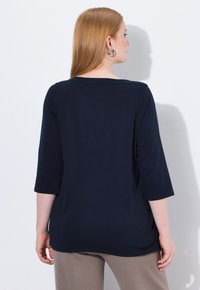 Top blu navy con maniche a tre quarti in morbido tessuto, scollo rotondo, vestibilità rilassata, caratterizzato da una texture liscia e un design minimale.