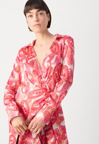 Robe à manches longues avec col, arborant un motif paisley rose vif. Fabriquée en tissu léger, avec un design croisé et un décolleté plongeant.