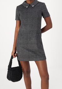 Kortärmad klänning i svart och grå rutmönster med krage, accentuerad med hjärtformade knappar, tillsammans med en texturerad svart vävd handväska.