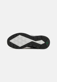 Black and white sneaker sole with textured rubber. Features an interlocking pattern and logo detail on the side. Green accent near the heel.
