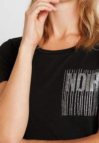 Black t-shirt with a round neckline, featuring a sparkling silver graphic on the left chest area, with vertical line patterns.