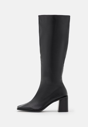 Zwarte kniehoog laars van soepel leer met een vierkante neus en een stevige hak, met een naadloos ontwerp en een strakke afwerking.