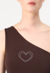 Rjava brezrokavnik s asimetričnim oblikovanjem, ki vključuje okrasitev v obliki srčka iz rhinestone-a na predelu prsnega koša. Mehak tekstilni material.