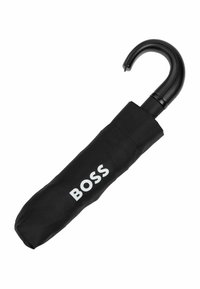 Crni kišobran pohranjen u odgovarajućem rukavu s bijelim logotipom "BOSS", s zakrivljenom crnom drškom i glatkom teksturom tkanine.