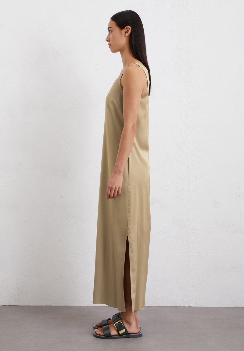 Satin, ärmelloses Maxikleid in Khaki mit einem seitlichen Schlitz. Kombiniert mit schwarzen Sandalen mit Schnallendetail. Glatte Textur und schlichtes Design.
