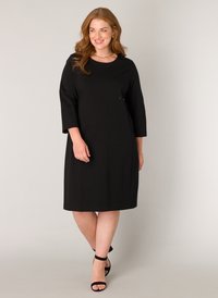 Zwarte jurk tot de knie met driekwart mouwen, gemaakt van zachte stof. Eenvoudig ontwerp met een ronde halslijn en zonder zichtbare patronen.