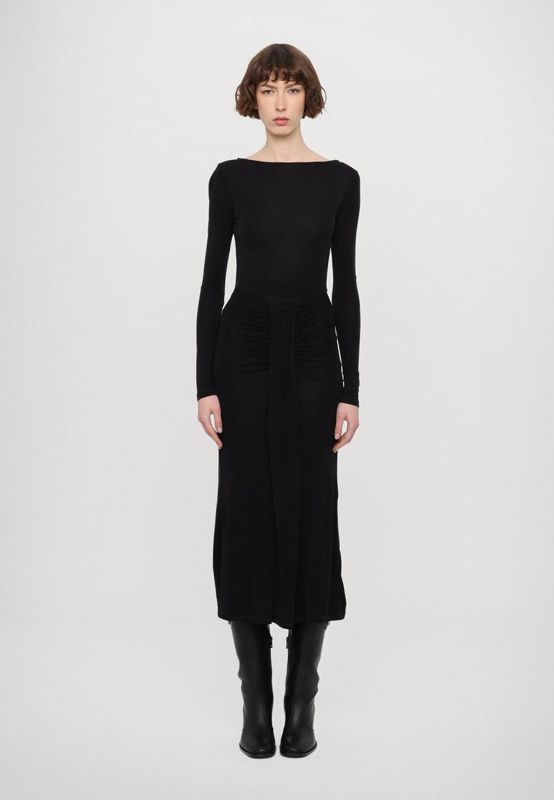 Vestido negro de manga larga con escote barco, detalle fruncido en la cintura y falda fluida. Llevado con botas negras hasta la rodilla.
