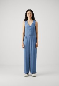 Šampanj jumpsuit z V-izrezom, sprednjim gumbom, brez rokavov, širokimi hlačnicami in sproščenim krojem, v svetlo modri barvi.