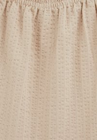 Tissu beige avec une texture tricotée, présentant des côtes verticales et de petits points en relief, froncé en haut avec un élastique.