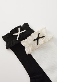 Chaussettes noires et blanches montantes avec des bordures froncées ; la chaussette noire arbore un nœud blanc, tandis que la chaussette blanche présente un nœud noir.