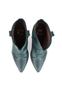 Botines de cuero en color verde azulado con punta afilada, que presentan un diseño ondulado, detalles de costura y pequeñas lengüetas en el talón.