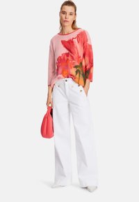 Floral knit sweater in pink and orange hues, paired with high-waisted white wide-leg pants and a small coral handbag.