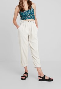 Blommig crop top i teal, matchad med krämfärgade manchesterbyxor med veck. Svarta remsandaler. Byxorna har uppvikta fållar och två framfickor.