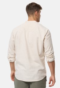 Camicia di lino beige chiaro con maniche lunghe, polsini arrotolati e orlo dritto. Design semplice con una cucitura della spalla posteriore e dettagli minimi.