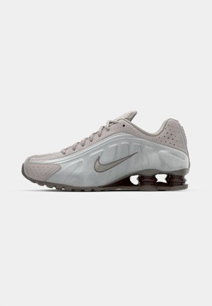 Chaussure de course Nike en gris clair avec une texture lisse, un design courbé et des ressorts de coussinage visibles en marron foncé au niveau du talon.